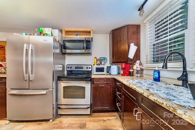 kitchen with light stone counters, rail lighting, light wood-style flooring, appliances with stainless steel finishes, and dark brown cabinetry