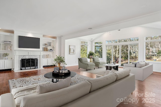 living room with hardwood / wood-style floors, crown molding, built in features, and a premium fireplace