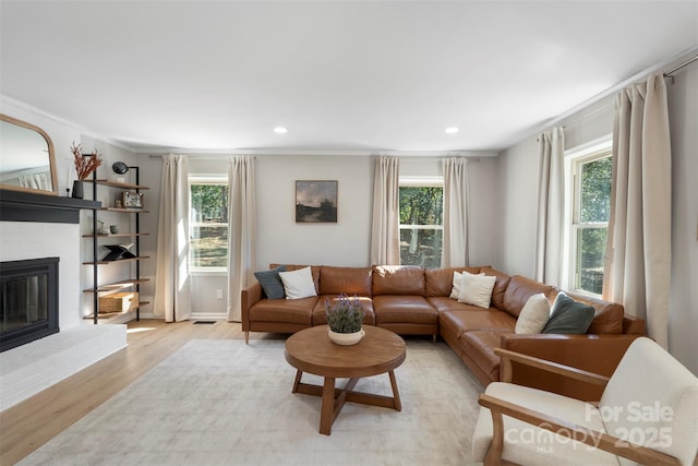 living area with ornamental molding, light wood-type flooring, a brick fireplace, and recessed lighting