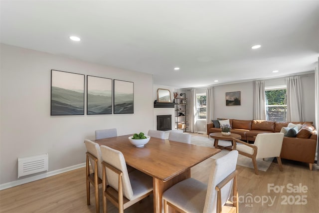 dining room with light wood-style floors, recessed lighting, visible vents, and a glass covered fireplace