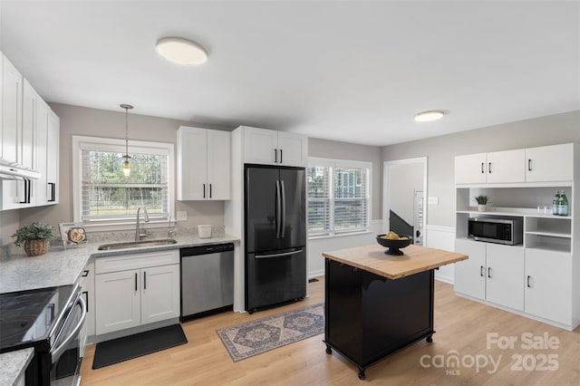 kitchen with light wood finished floors, appliances with stainless steel finishes, white cabinets, and a sink