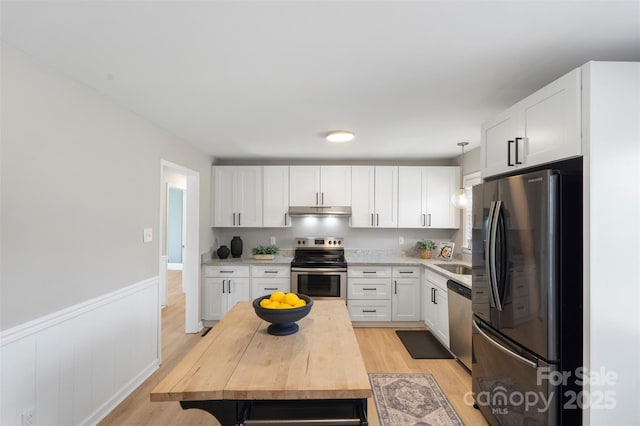 kitchen with light wood-style floors, a wainscoted wall, stainless steel appliances, under cabinet range hood, and white cabinetry