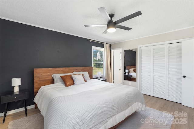 bedroom with light wood finished floors, ceiling fan, ornamental molding, a textured ceiling, and a closet