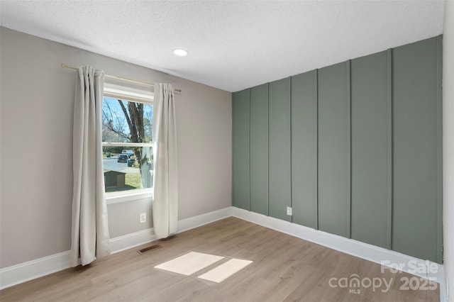 empty room featuring light wood finished floors, baseboards, visible vents, and a textured ceiling