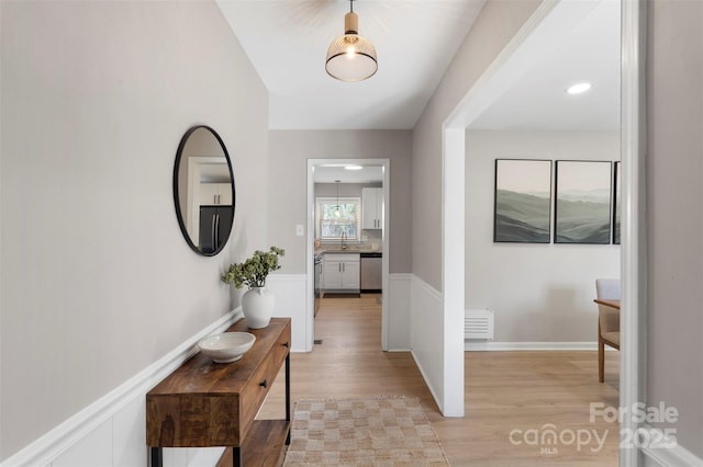 hallway featuring wainscoting, a sink, and light wood finished floors