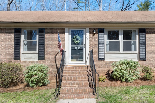 entrance to property featuring brick siding and roof with shingles