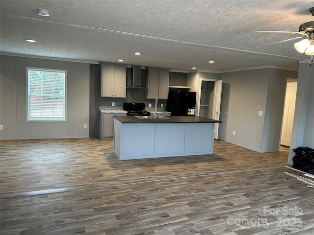 kitchen featuring black appliances, gray cabinets, a kitchen island with sink, and wall chimney range hood