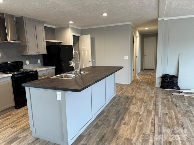 kitchen with gray cabinetry, wall chimney exhaust hood, an island with sink, and black appliances