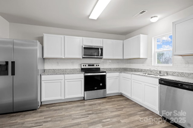 kitchen with white cabinets, light stone countertops, stainless steel appliances, light wood-style floors, and a sink