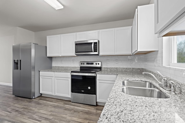 kitchen with stainless steel appliances, wood finished floors, a sink, white cabinets, and tasteful backsplash