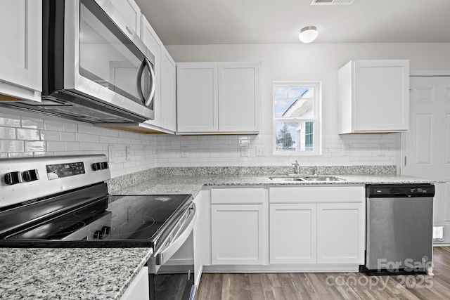 kitchen with stainless steel appliances, white cabinets, a sink, and light wood-style flooring