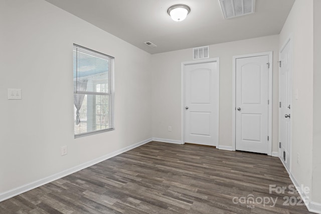 unfurnished bedroom with visible vents, dark wood finished floors, and baseboards