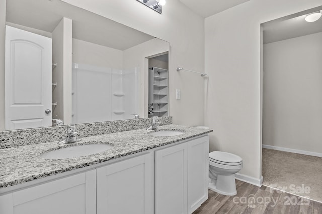 bathroom with toilet, double vanity, baseboards, and a sink