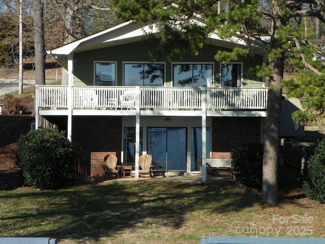 back of house featuring a balcony, a lawn, and brick siding