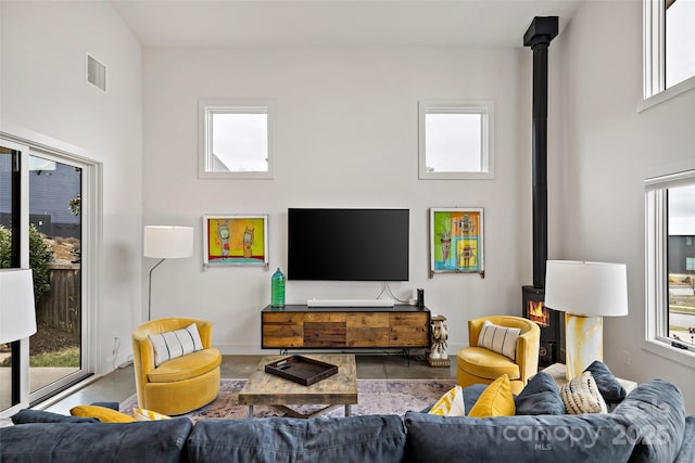 living room with a wood stove, visible vents, plenty of natural light, and a towering ceiling