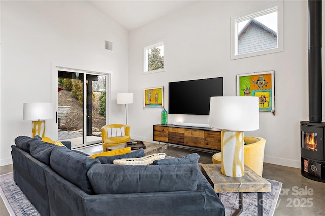 living room with a wood stove, visible vents, high vaulted ceiling, and baseboards