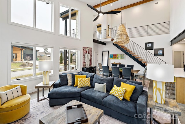 living room with stairway, a high ceiling, wood finished floors, baseboards, and ceiling fan with notable chandelier