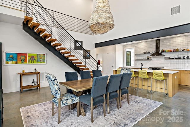 dining room with concrete flooring, visible vents, a high ceiling, and stairs