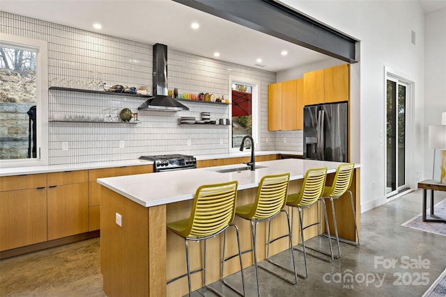 kitchen featuring a kitchen island with sink, finished concrete floors, black refrigerator with ice dispenser, wall chimney range hood, and open shelves