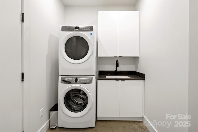 clothes washing area featuring baseboards, cabinet space, a sink, and stacked washing maching and dryer