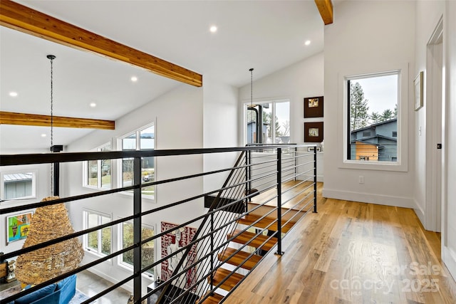 hallway featuring beam ceiling, a healthy amount of sunlight, light wood finished floors, and an upstairs landing