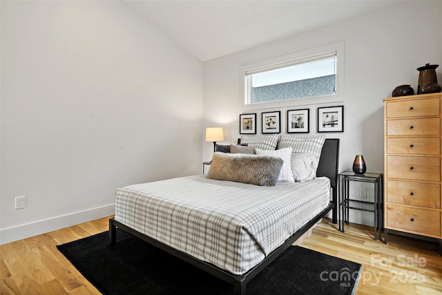 bedroom with lofted ceiling, light wood-style floors, and baseboards