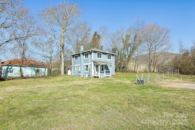 rear view of house featuring covered porch, a lawn, and a chimney