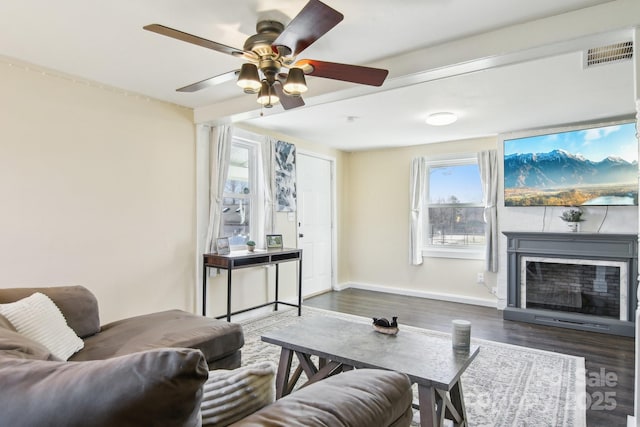 living room featuring a glass covered fireplace, visible vents, baseboards, and wood finished floors