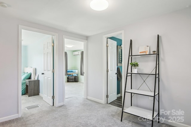 hall featuring a wall mounted air conditioner, visible vents, baseboards, and carpet flooring