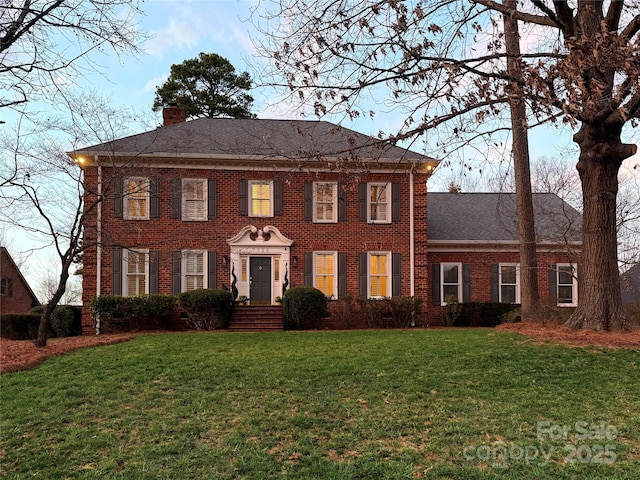 colonial inspired home featuring brick siding, a chimney, and a front yard