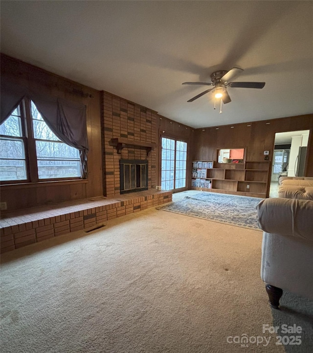 unfurnished living room with a healthy amount of sunlight, carpet floors, a fireplace, and wood walls