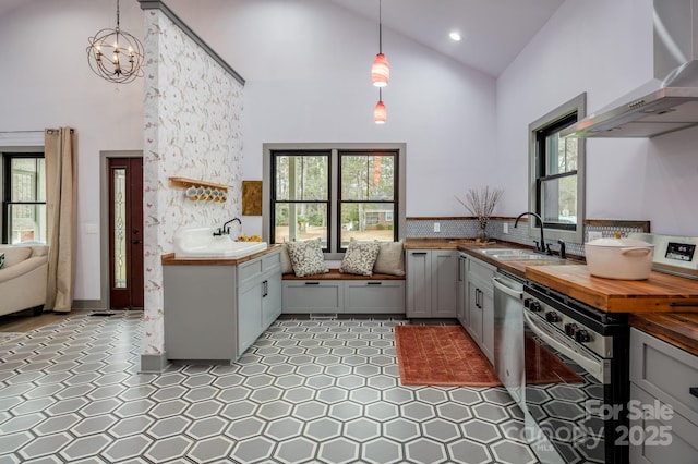 kitchen with wall chimney exhaust hood, sink, decorative light fixtures, high vaulted ceiling, and stainless steel appliances