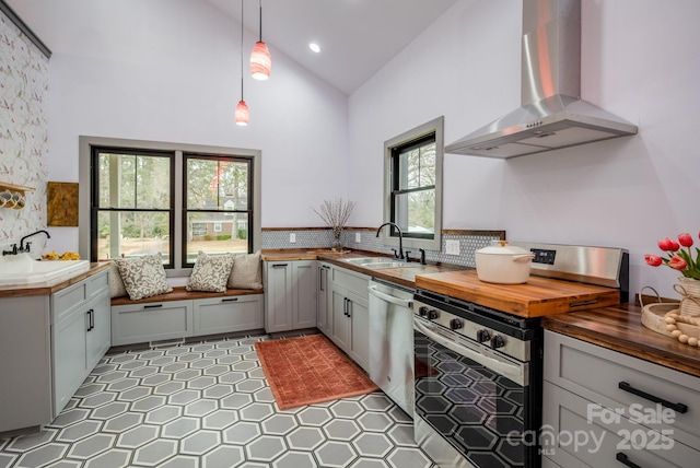 kitchen with wood counters, sink, pendant lighting, stainless steel appliances, and wall chimney range hood