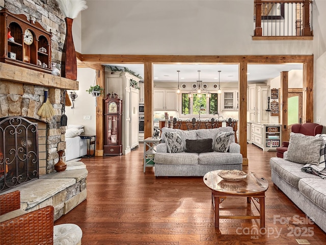 living room with dark wood-type flooring, a towering ceiling, a fireplace, and a chandelier