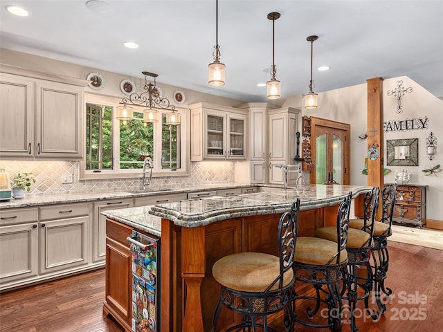 kitchen with decorative light fixtures, light stone countertops, and a center island with sink