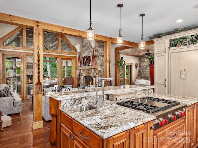 kitchen with pendant lighting, sink, stainless steel gas cooktop, a center island with sink, and a stone fireplace