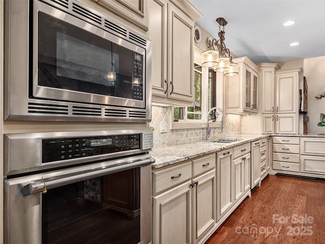 kitchen with sink, appliances with stainless steel finishes, pendant lighting, light stone countertops, and cream cabinetry