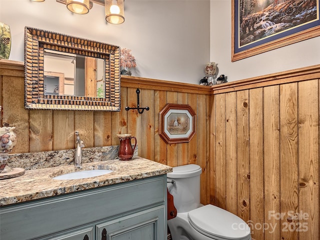 bathroom featuring wooden walls, vanity, and toilet