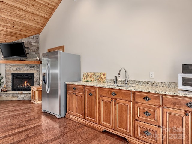 kitchen featuring sink, dark hardwood / wood-style floors, stainless steel refrigerator with ice dispenser, light stone counters, and a stone fireplace