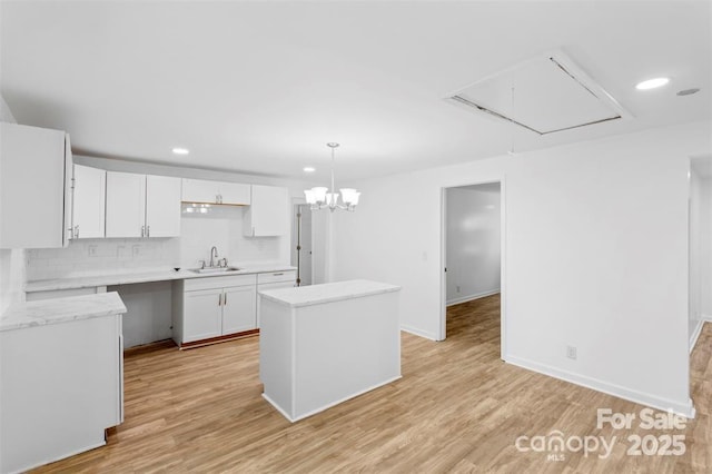 kitchen with a kitchen island, pendant lighting, white cabinetry, sink, and light hardwood / wood-style floors