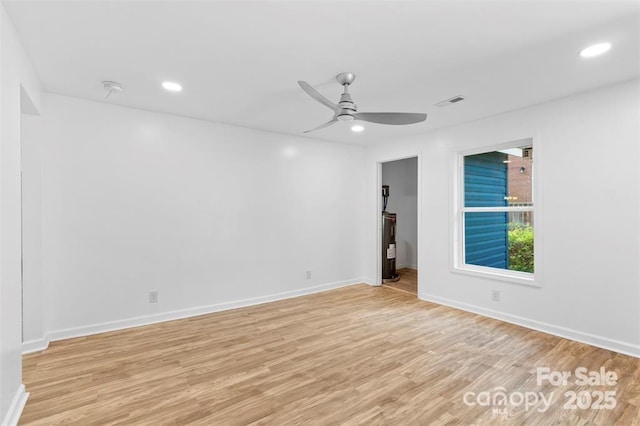 spare room with water heater, ceiling fan, and light hardwood / wood-style flooring