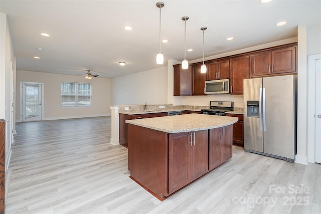 kitchen featuring stainless steel appliances, light wood finished floors, hanging light fixtures, ceiling fan, and open floor plan