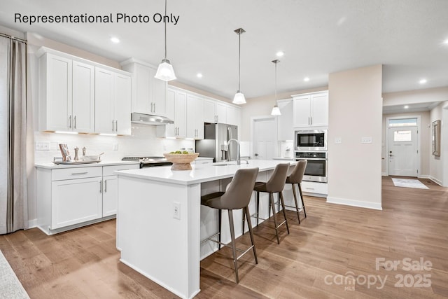 kitchen featuring sink, an island with sink, pendant lighting, stainless steel appliances, and white cabinets