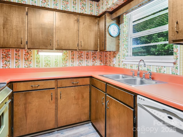 kitchen featuring white dishwasher, light countertops, brown cabinets, and a sink