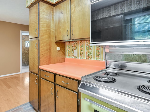 kitchen with baseboards, light wood-type flooring, light countertops, brown cabinets, and range
