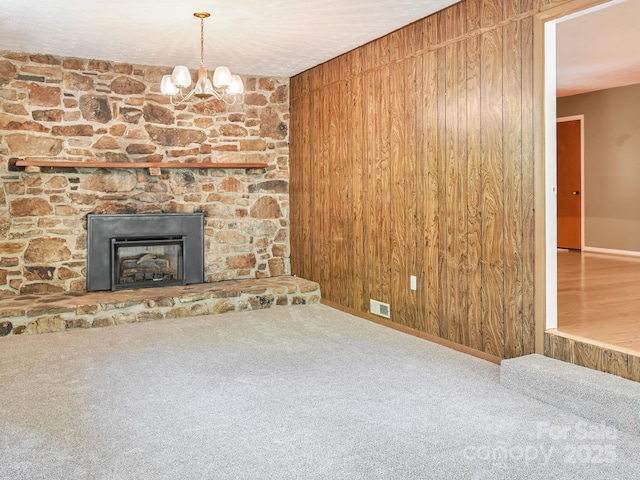unfurnished living room featuring a notable chandelier, carpet floors, a stone fireplace, baseboards, and visible vents
