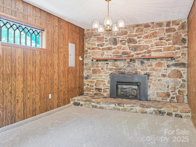 unfurnished living room featuring an inviting chandelier, carpet floors, wood walls, and a stone fireplace