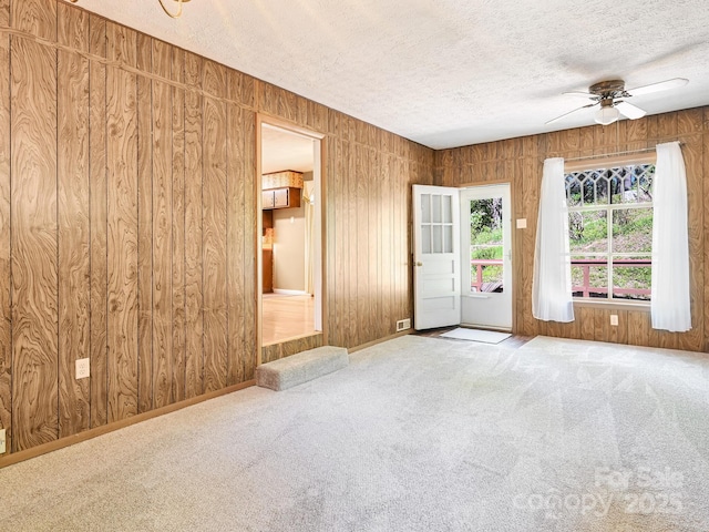 carpeted empty room with wooden walls, ceiling fan, and a textured ceiling