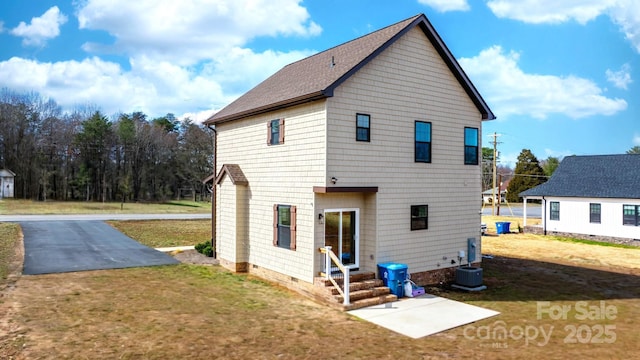 rear view of property featuring a yard, roof with shingles, and central air condition unit