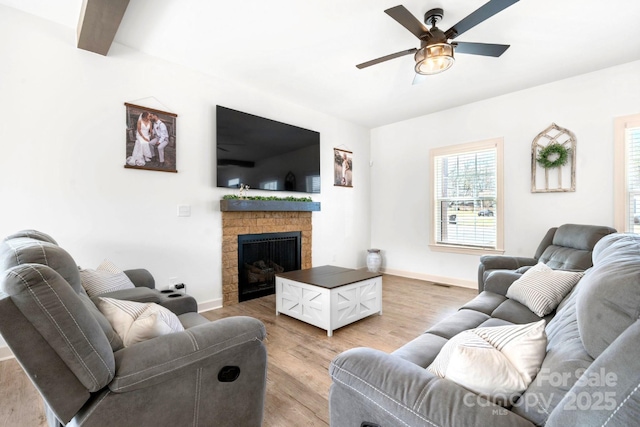 living area featuring baseboards, ceiling fan, a fireplace, and light wood-style floors